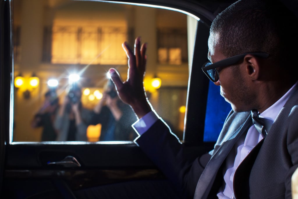 Celebrity in limousine waving at paparazzi photographers