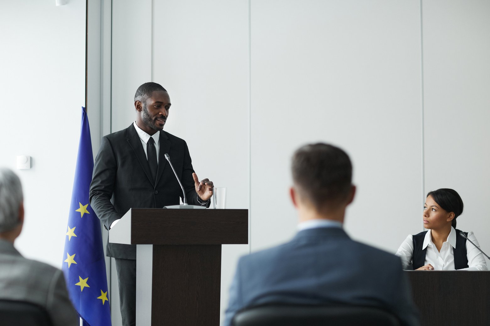 A Man in Black Suit Speaking in Front of People